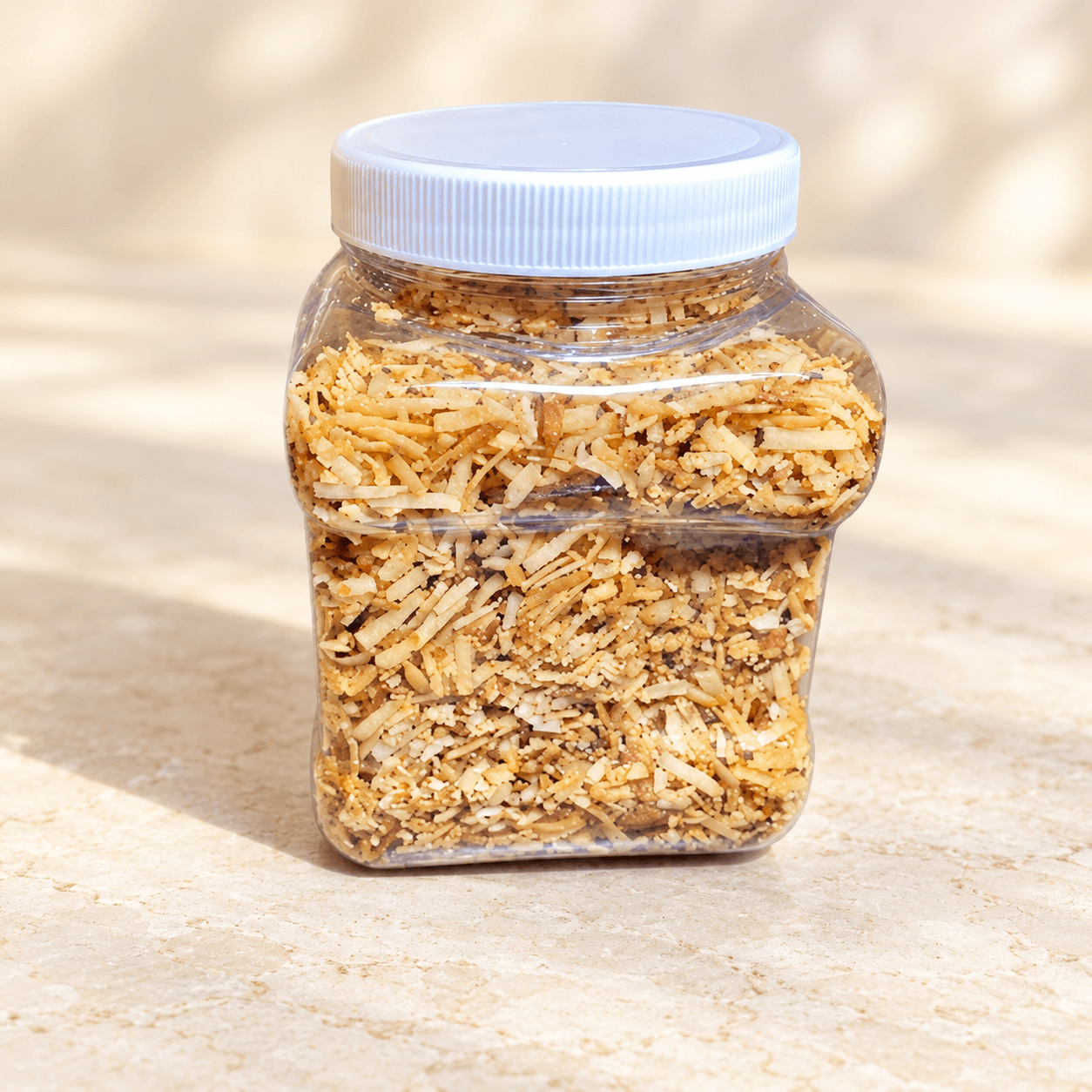 A white-lidded jar of golden Coconut Candy Crunch on a warm stone counter.