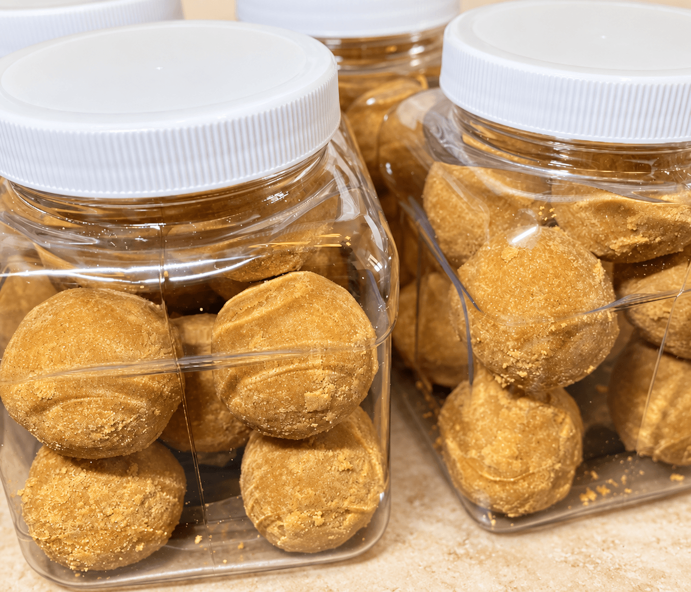 Jars of rounded golden Donkwa bites on a warm stone counter.